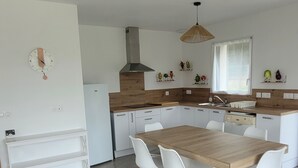 A modern kitchen with a wooden dining table, white chairs, and a built-in oven. - Spacious single-story house (Villeneuve-en-Retz)