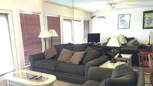 Ein Wohnzimmer mit einer Couch, Sesseln, einem Couchtisch, Lampen, einem Fernseher und Kunstwerken an der Wand.