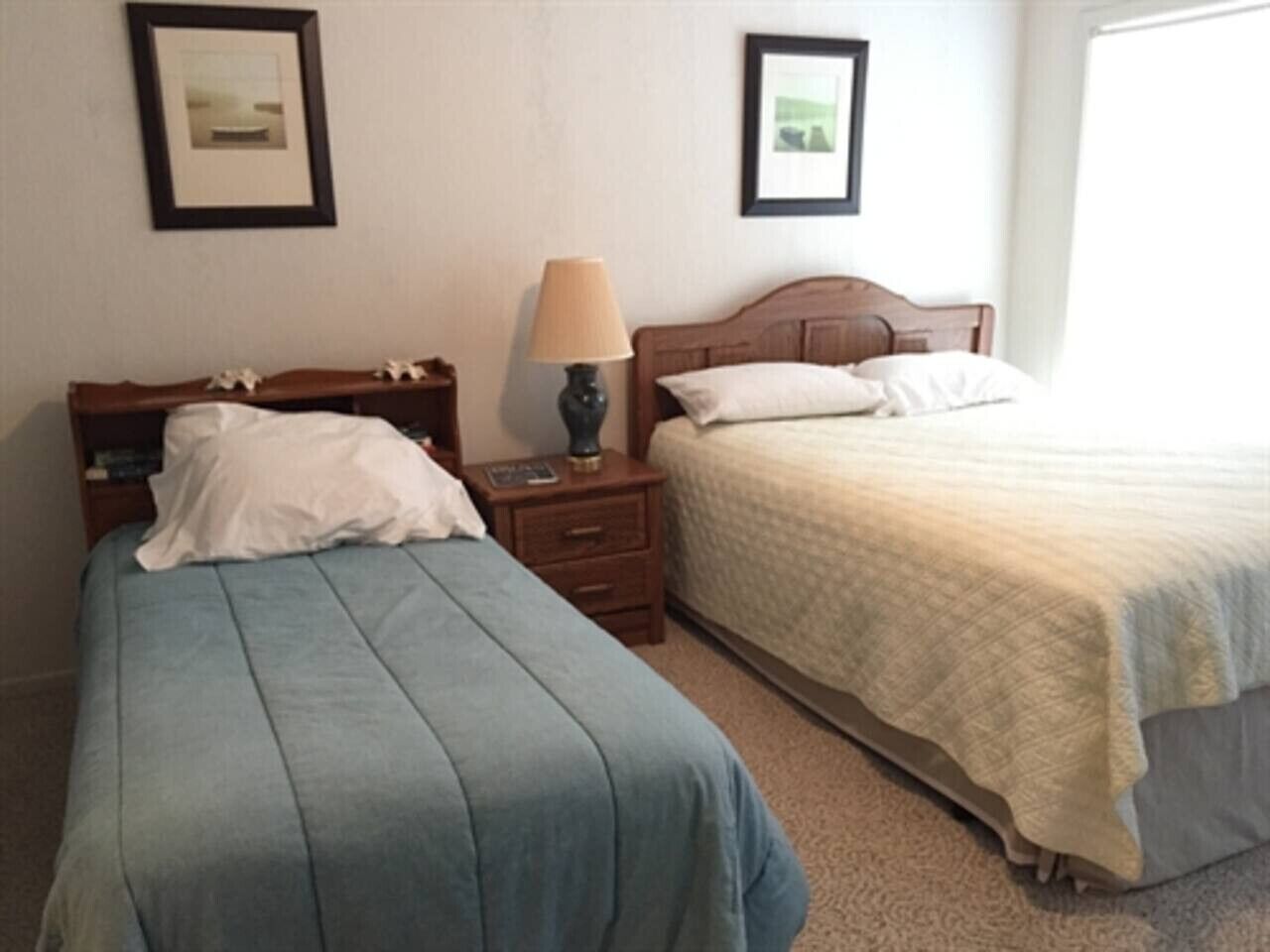 Two single beds with wooden headboards, a nightstand with a lamp, and framed pictures on the walls.