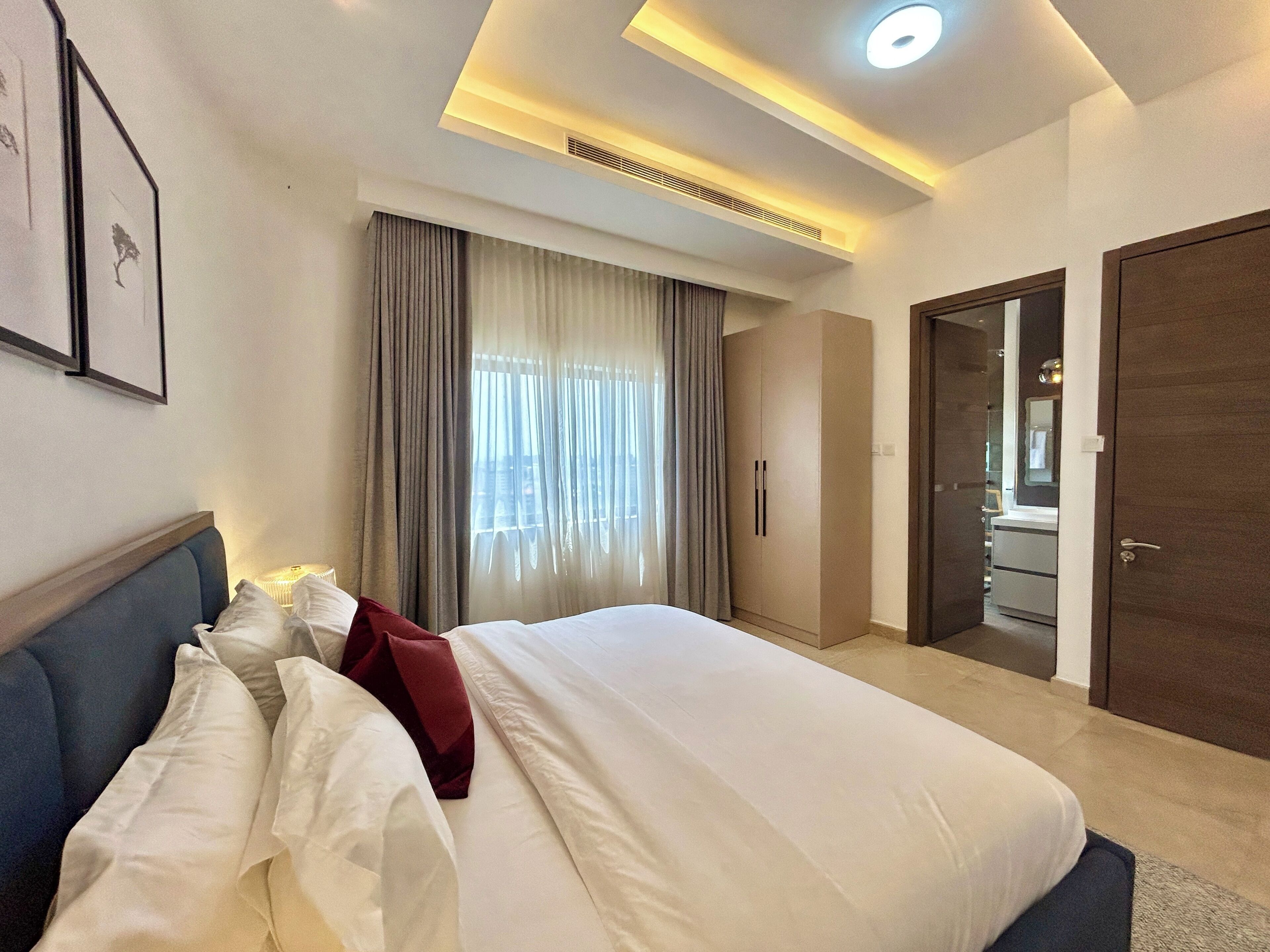 A hotel room with a bed, curtains, a wardrobe, and a bathroom visible through an open door.