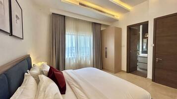 A hotel room with a bed, curtains, a wardrobe, and a bathroom visible through an open door.