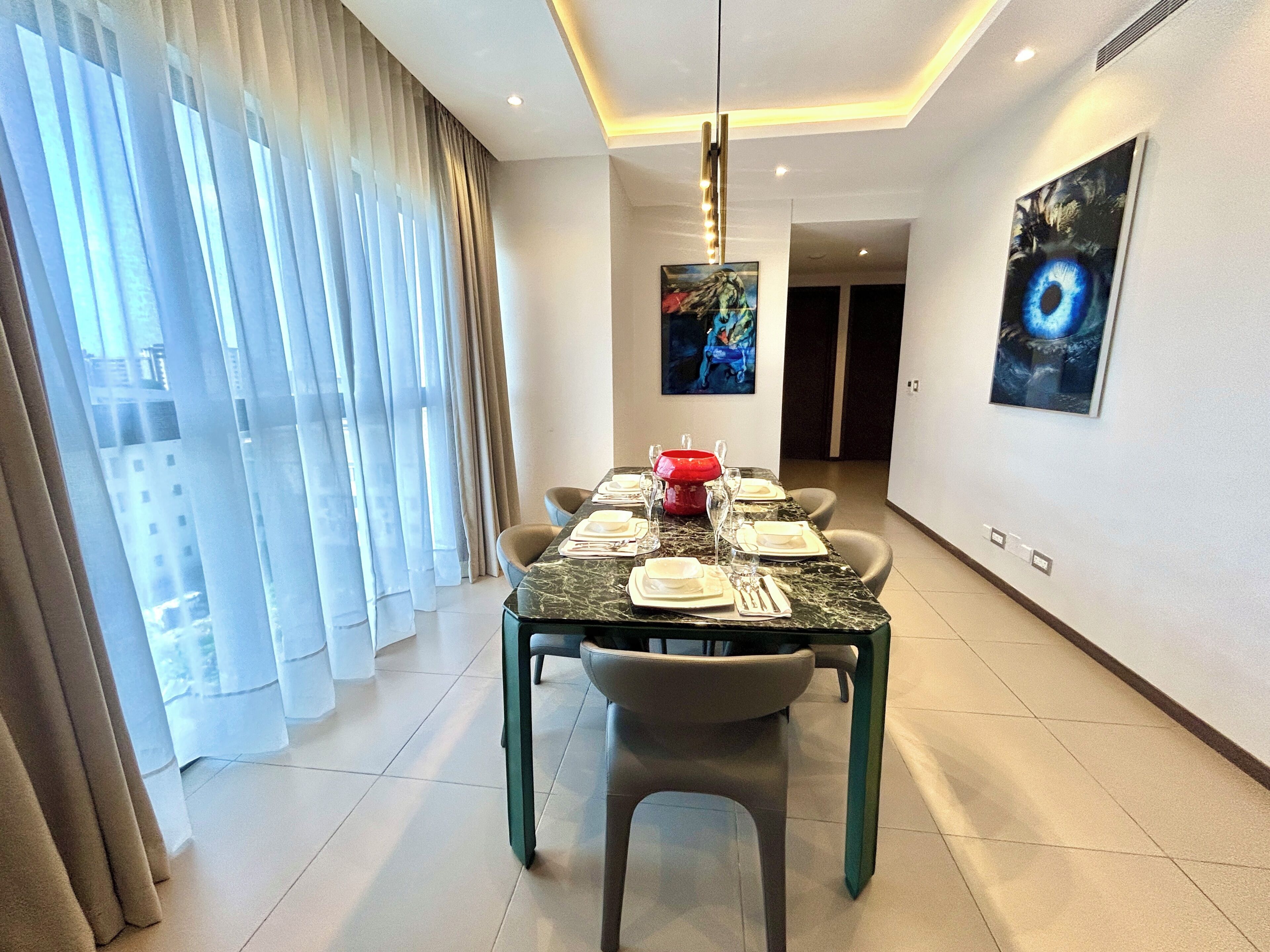 A dining area with a table set for four, a modern chandelier, and artwork on the walls.