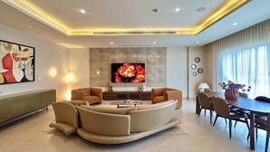 A modern living room with a curved sofa, a flat-screen TV, a dining table with chairs, and a large window with curtains. - Riverrun Residence (Lagos)