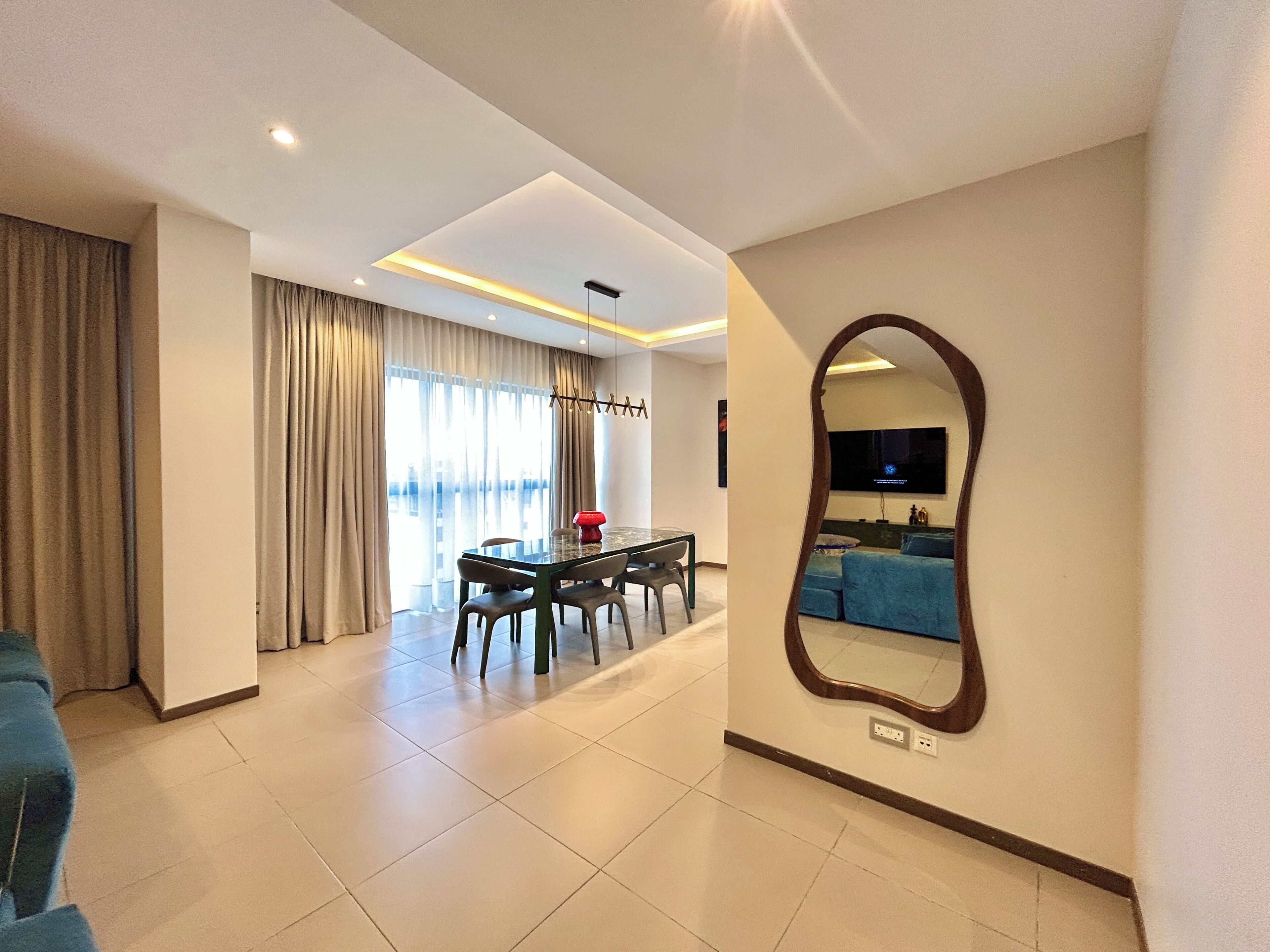 A modern living room with a dining area, a large mirror, and a flat-screen TV mounted on the wall.