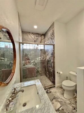 Een badkamer met een marmeren wastafel, een douchecabine van glas en een toilet.