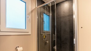 Eine gläserne Duschkabine mit sichtbarer Toilette durch das Glas, ein Handtuchhalter und ein Fenster über der Toilette.