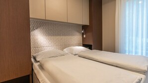 Ein Hotelzimmer mit zwei Betten, einem gemusterten Kopfteil, einer Nachttischlampe und einem Fenster mit durchsichtigen Vorhängen.