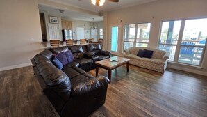 A spacious living room with a large leather sofa, a smaller sofa, and a coffee table. There is a ceiling fan and a view of the kitchen and dining area through an open door. - Waterview Home with Two Private Boat Lifts (Port O`Connor)