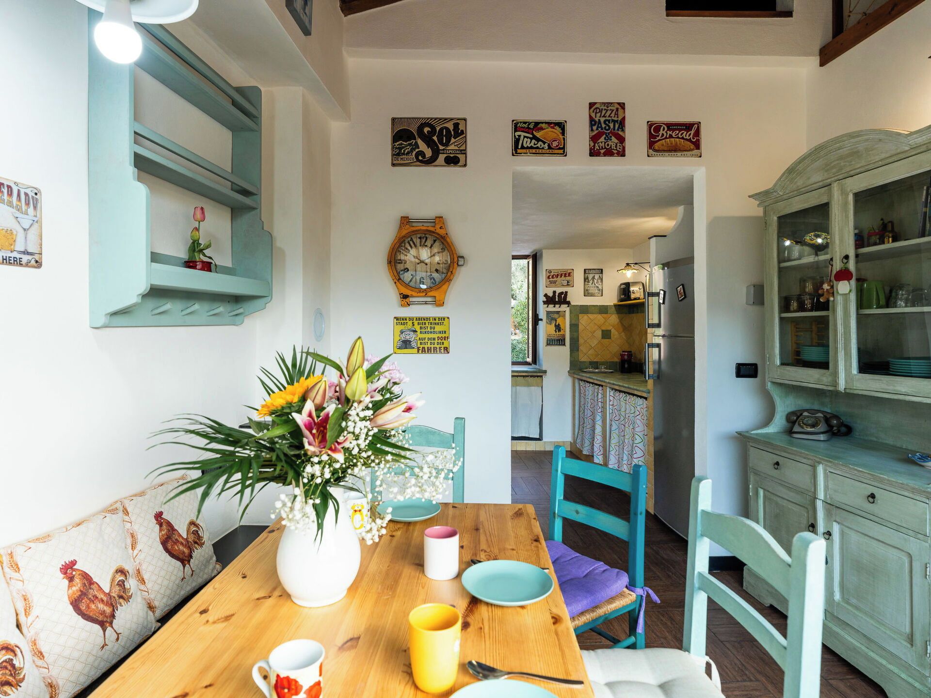A dining area with a wooden table, chairs, a vase with flowers, and a clock on the wall.