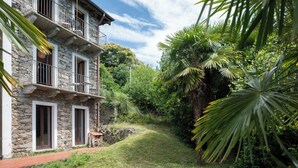 Un edificio de piedra con balcón, rodeado de exuberante vegetación y un sendero.