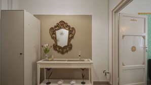 Een badkamer met een witte wastafel, een decoratieve spiegel, een vaas met bloemen, en een deur met een decoratieve knop.