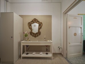 Ein Badezimmer mit einem weißen Waschtisch, einem Zier-Spiegel, einer Vase mit Blumen und einer Tür mit dekorativer Griff.