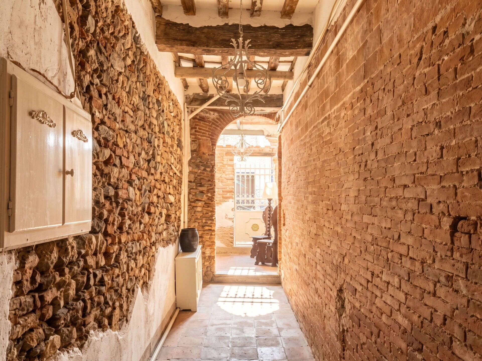 A narrow corridor with stone walls, a wooden door, and a chandelier.