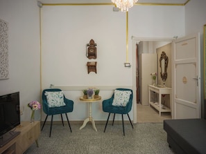 Ein Zimmer mit zwei türkisfarbenen Sesseln, einem kleinen runden Tisch, einem Fernseher und einem Bett.