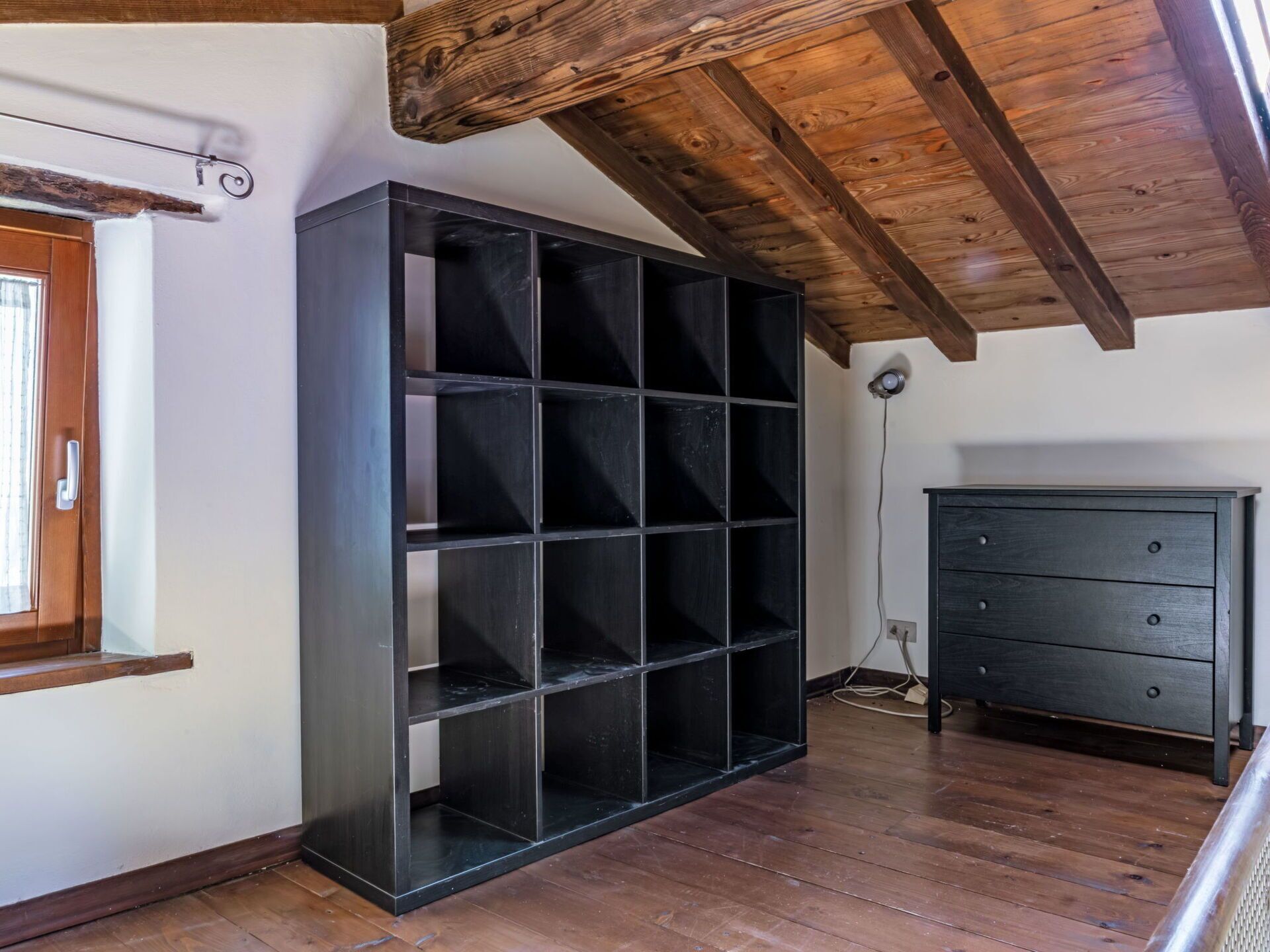 Ein Zimmer mit einem großen schwarzen Regalsystem, einer Holzschrank und einer Holzbalkendecke.