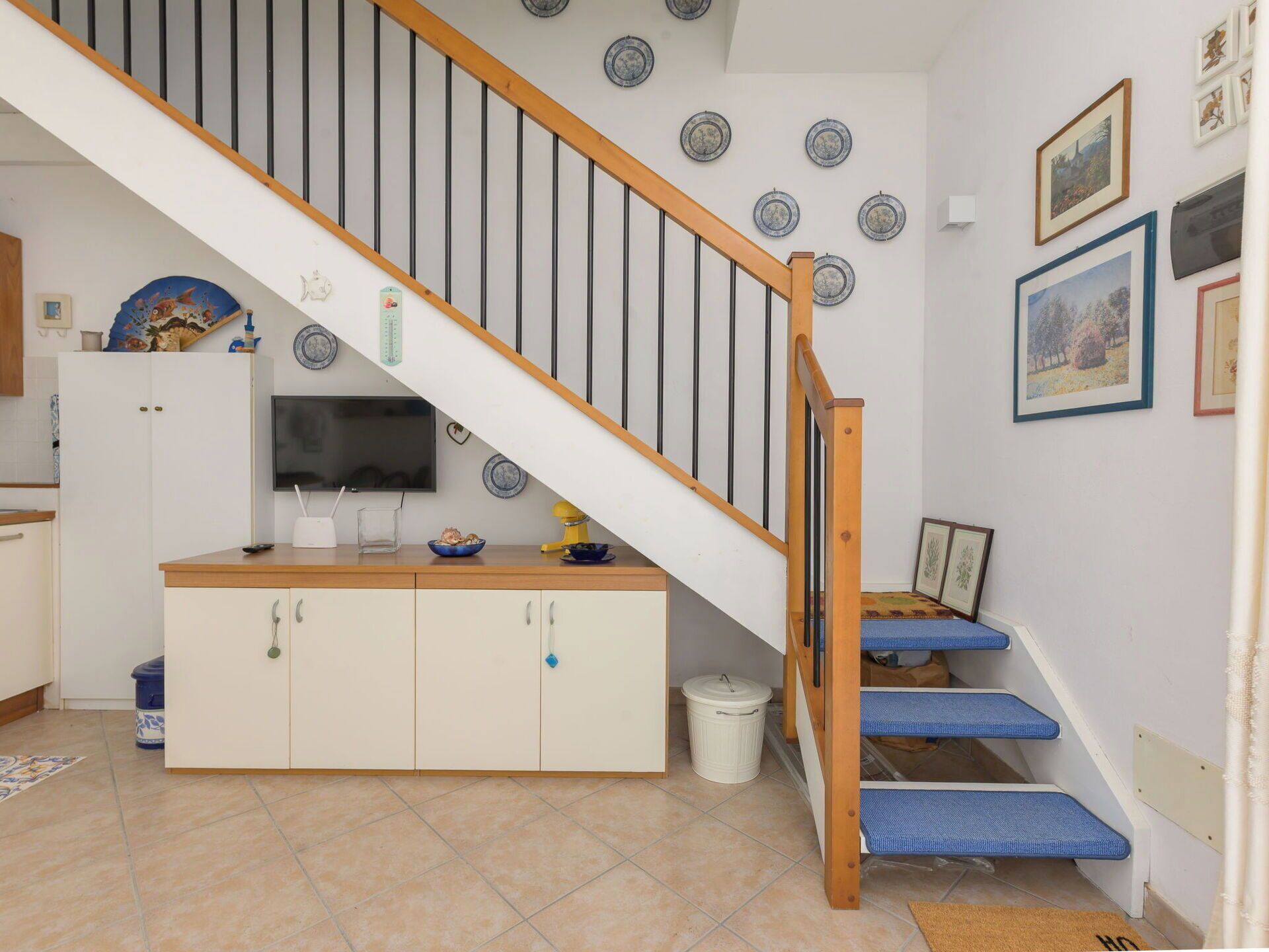 A kitchen with a wooden staircase, a TV, and various kitchen appliances.