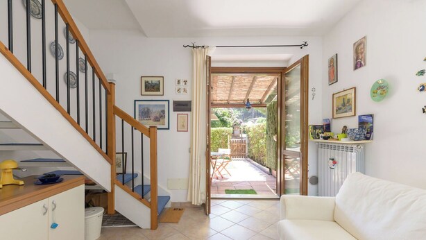 Un interior d'habitatge amb una escala, un sofà blanc, zona de menjador i vista a un jardí exterior.