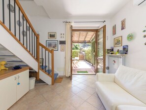 A home interior with a staircase, a white couch, a dining area, and a view to an outdoor garden. - Beautiful apartment for 3 people with WIFI, A/C, terrace and pets allowed (Castiglione Della Pescaia)