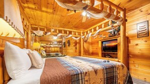 Une chambre dans un chalet en bois, équipée d’un lit, d’une télévision et d’un ventilateur de plafond.