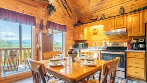 Une cabane en bois comprenant un coin repas, une cuisine et de grandes fenêtres donnant sur un paysage montagneux.