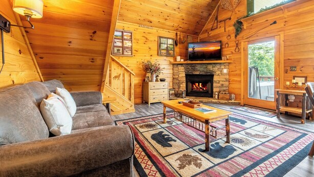 L’intérieur d’une cabane en rondins, avec une cheminée, des murs en bois, un canapé et un téléviseur.