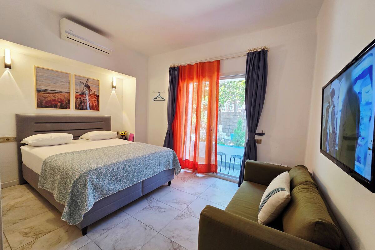 A bedroom with a bed, a sofa, a TV, and a window with curtains.