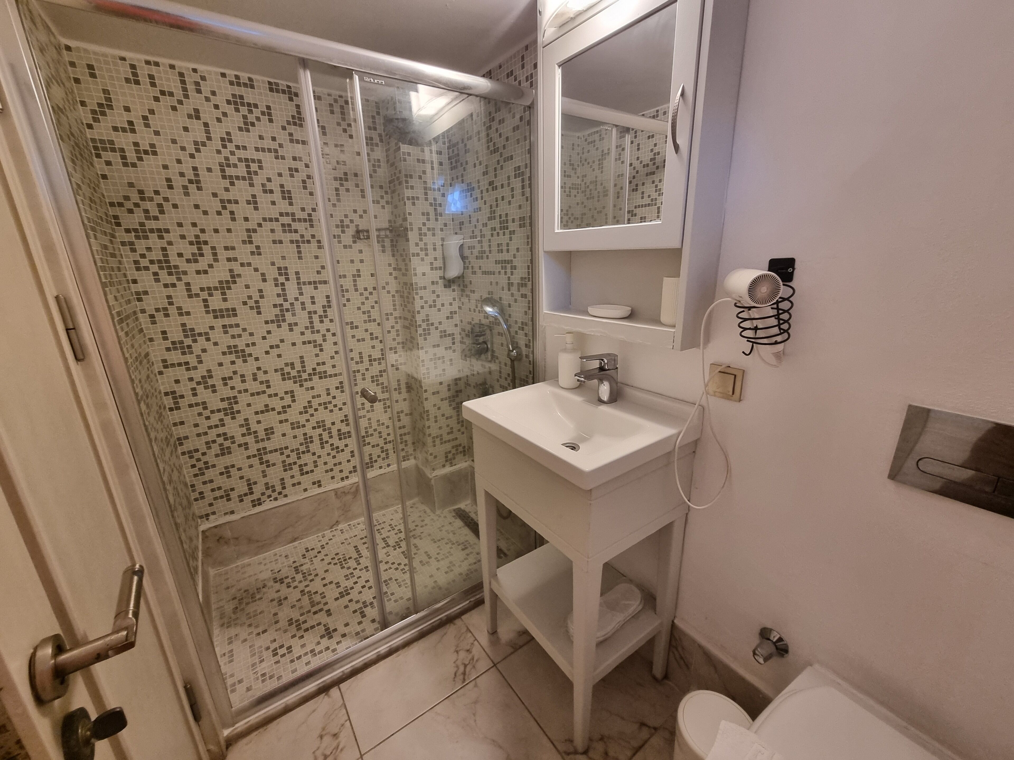 Un bany amb plat de dutxa de vidre, un lavabo blanc i un vàter.