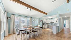 Une cuisine spacieuse équipée d’appareils modernes, un coin repas avec une table et des chaises en bois, et une vue sur l’extérieur grâce à de grandes fenêtres.