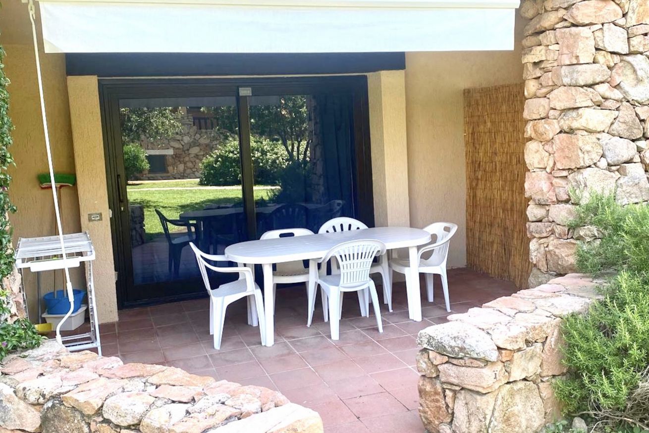 An outdoor patio with a table and chairs, a stone wall, and a view of a garden.
