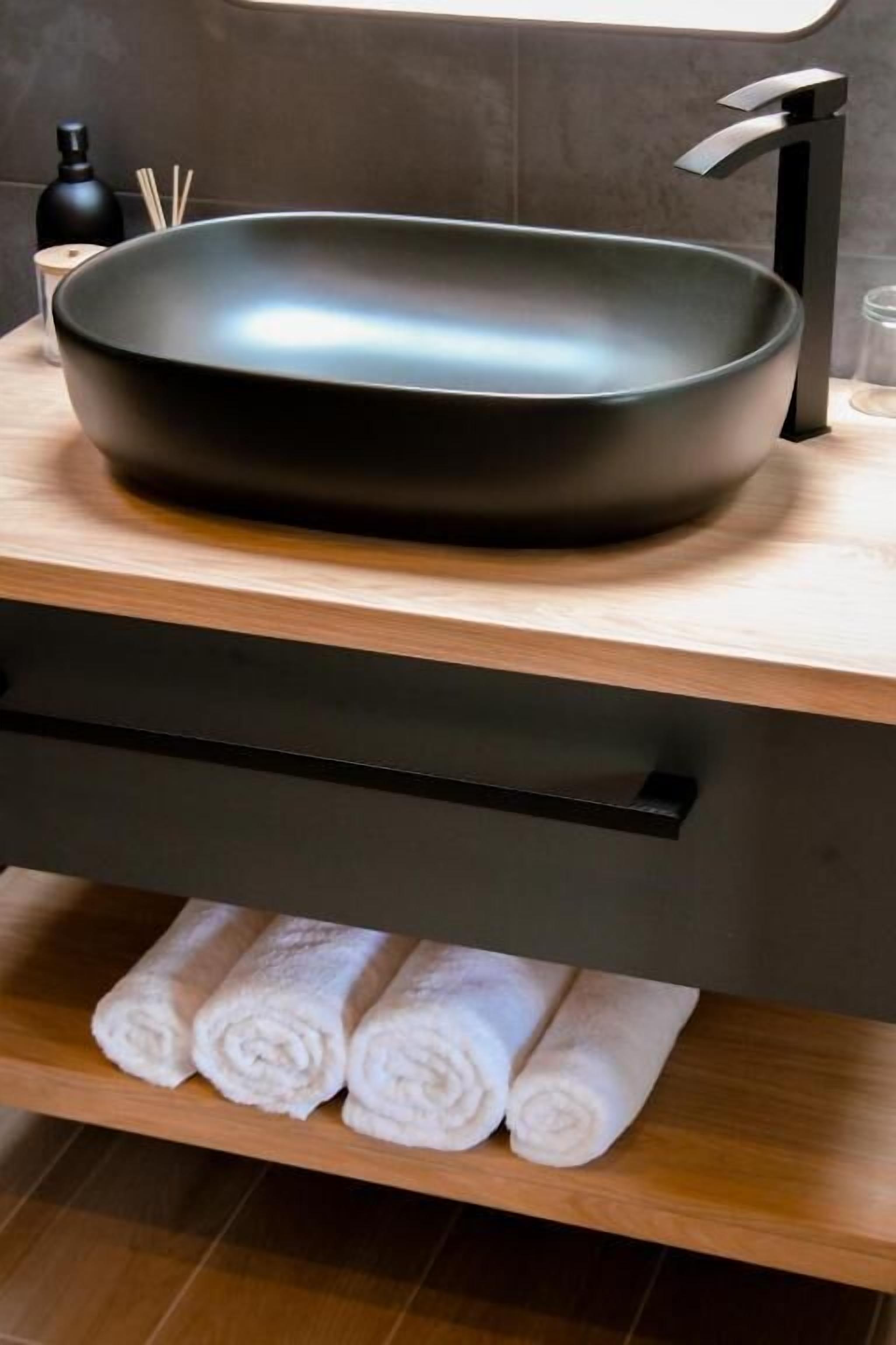 Een moderne badkamer met een zwarte wasbak, een houten aanrechtblad en een handdoekrek met opgerolde handdoeken.