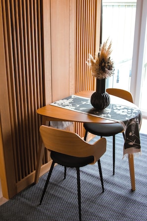 A wooden dining table with a vase of dried flowers, two chairs, and a patterned table runner. - M26 Prémium Apartmanház (Tihany)