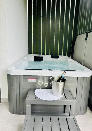 A hot tub with a metal bucket containing a bottle and glasses, a wooden table, and a metal chair.