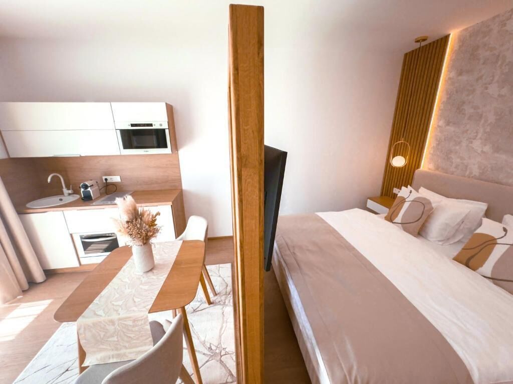 A modern hotel room with a bed, bedside table, and a small kitchenette.