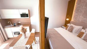 A modern hotel room with a bed, bedside table, and a small kitchenette.