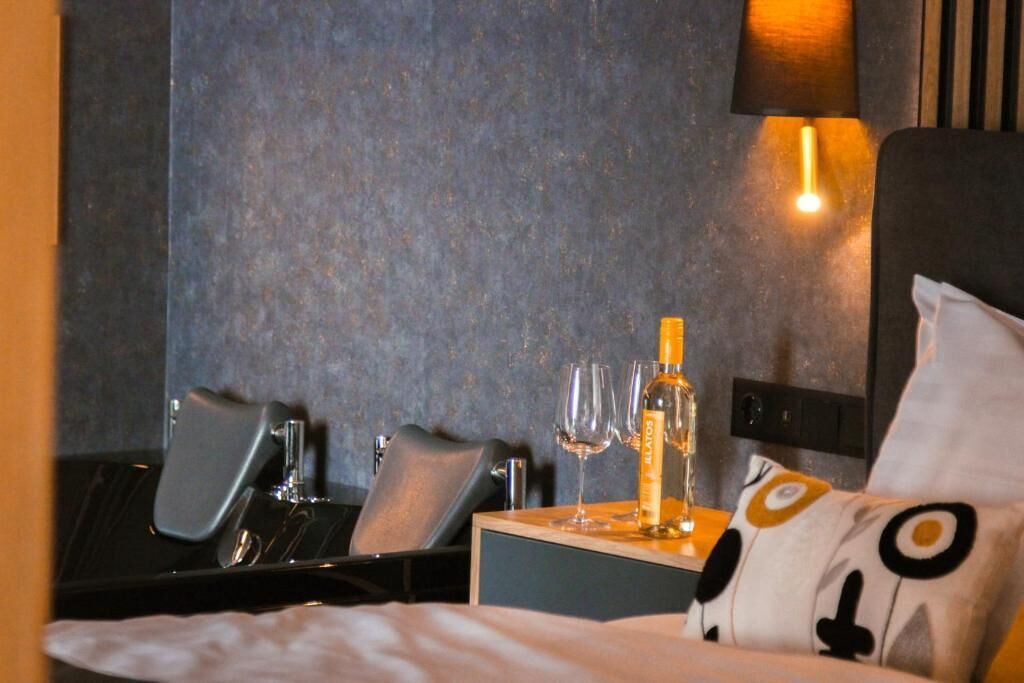 Et hotelværelse med en seng, et natbord med en flaske og glas, en stol og en lampe.