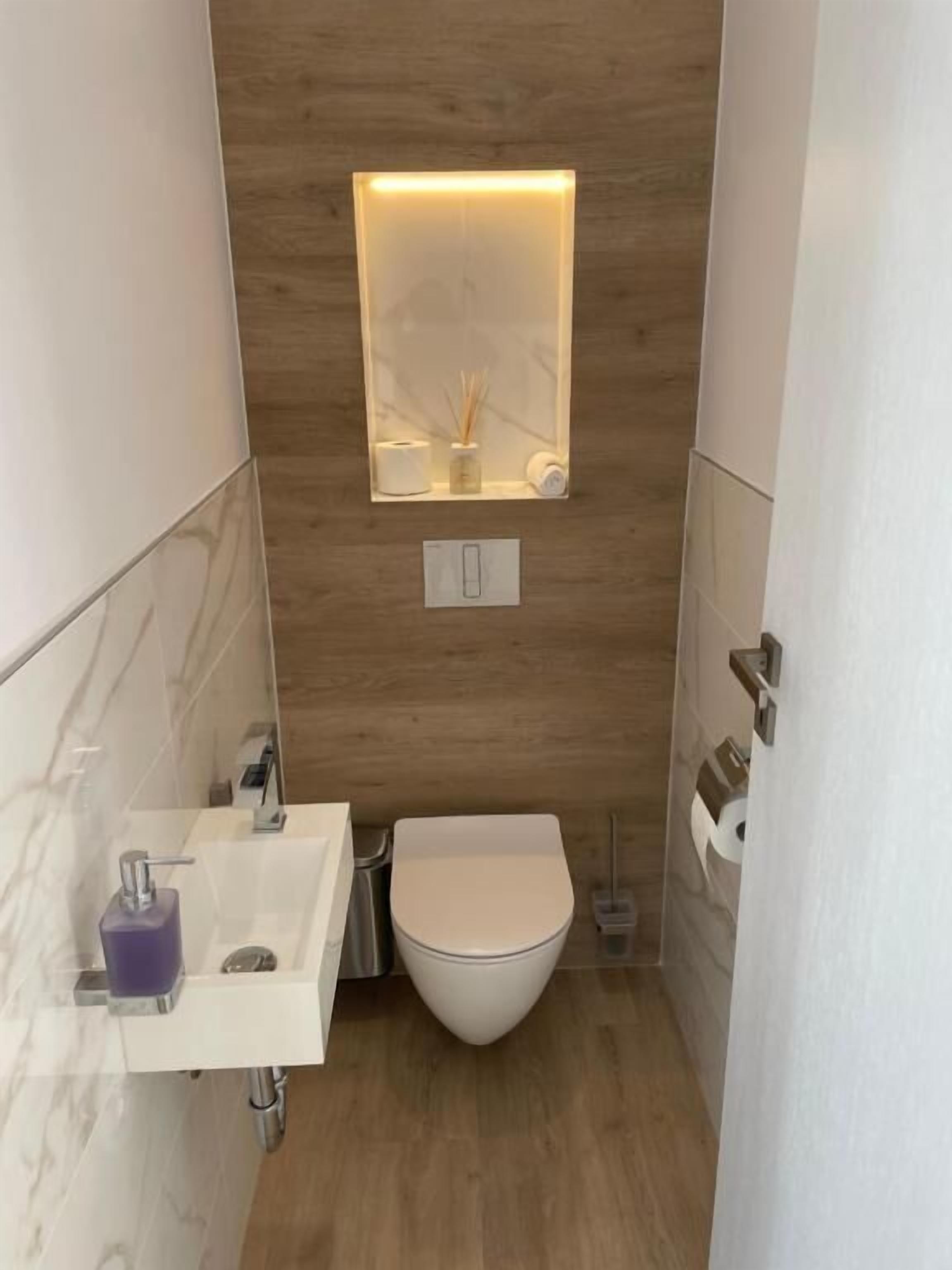 Un baño pequeño con un lavamanos blanco, un inodoro y un espejo con luz superior.