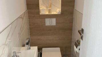 Un baño pequeño con un lavamanos blanco, un inodoro y un espejo con luz superior.