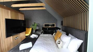 A modern hotel room with a large bed, a flat-screen TV, a desk with a chair, and a plant.