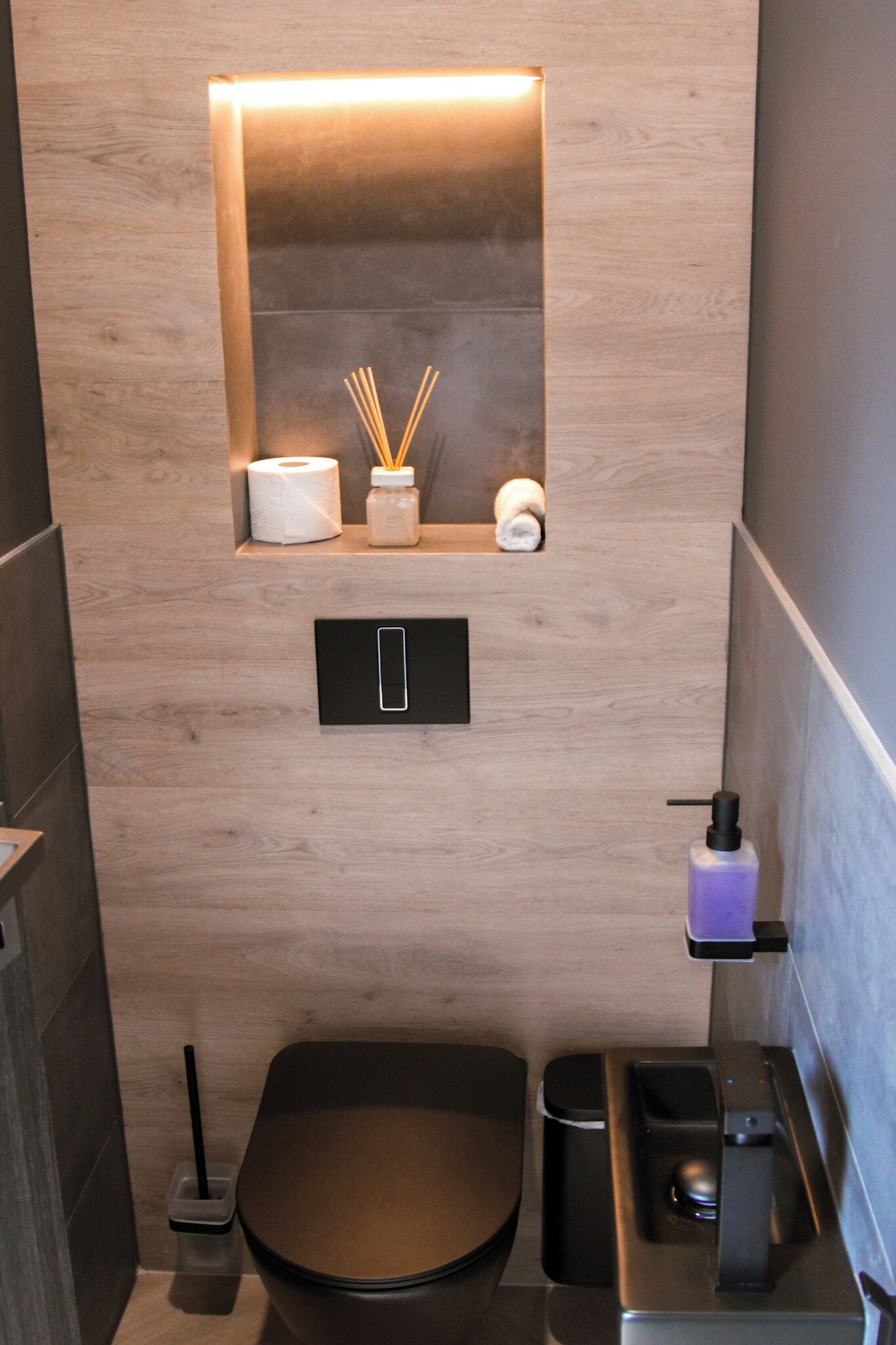 Un baño moderno con tocador de madera, inodoro, bidé y repisa con artículos de aseo.