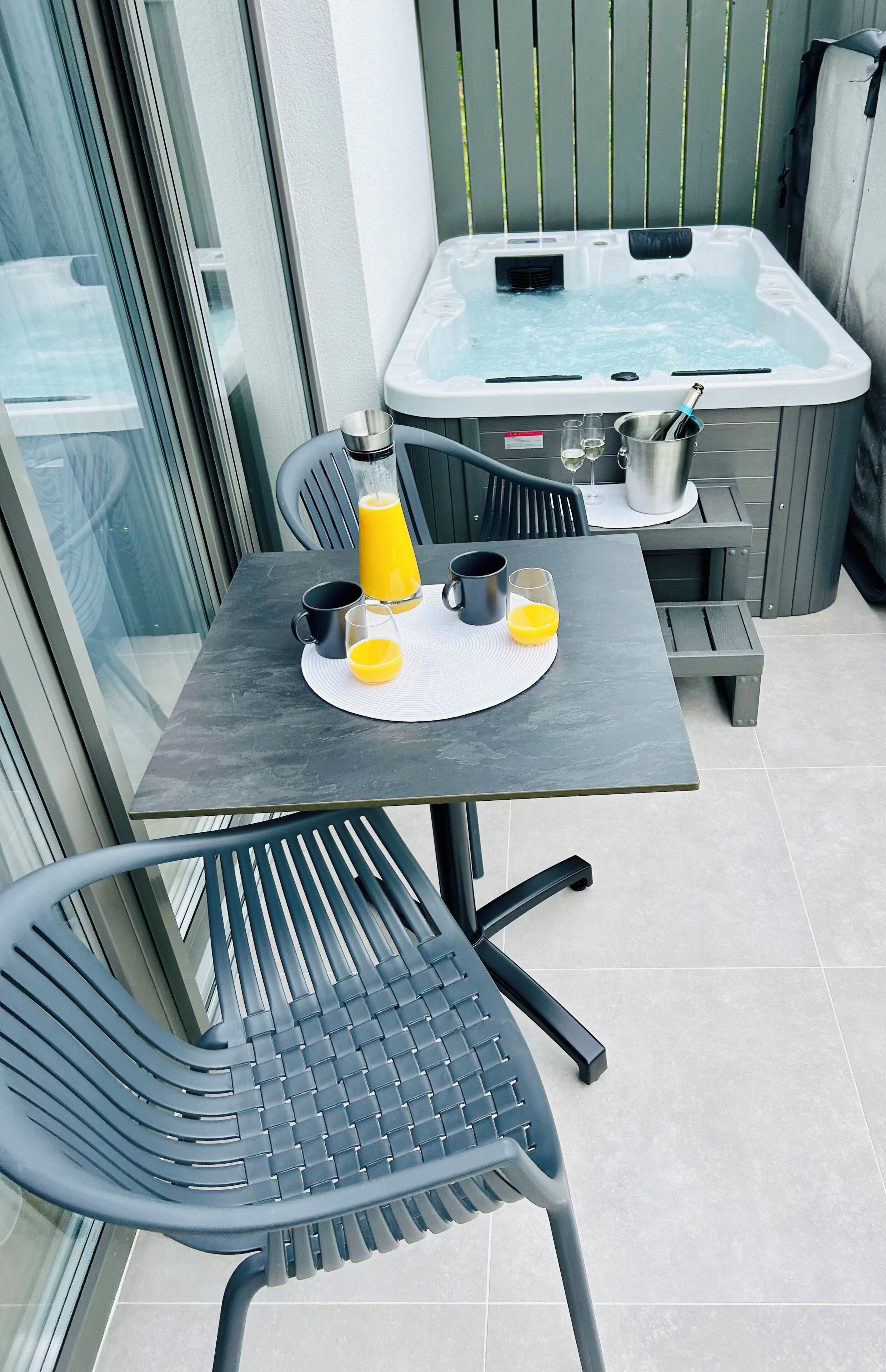 A balcony with a table, chairs, a hot tub, and a glass door.