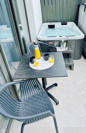 A balcony with a table, chairs, a hot tub, and a glass door.