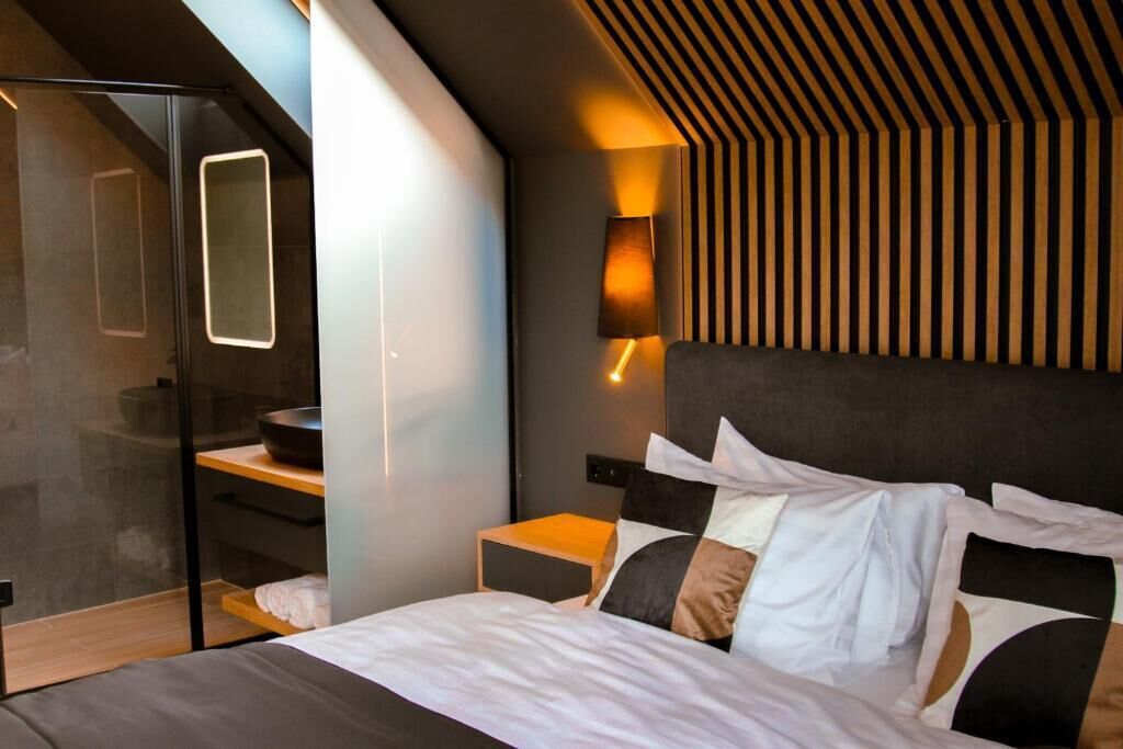A modern bedroom with a bed, bedside tables, a built-in bench, and a wall-mounted lamp.