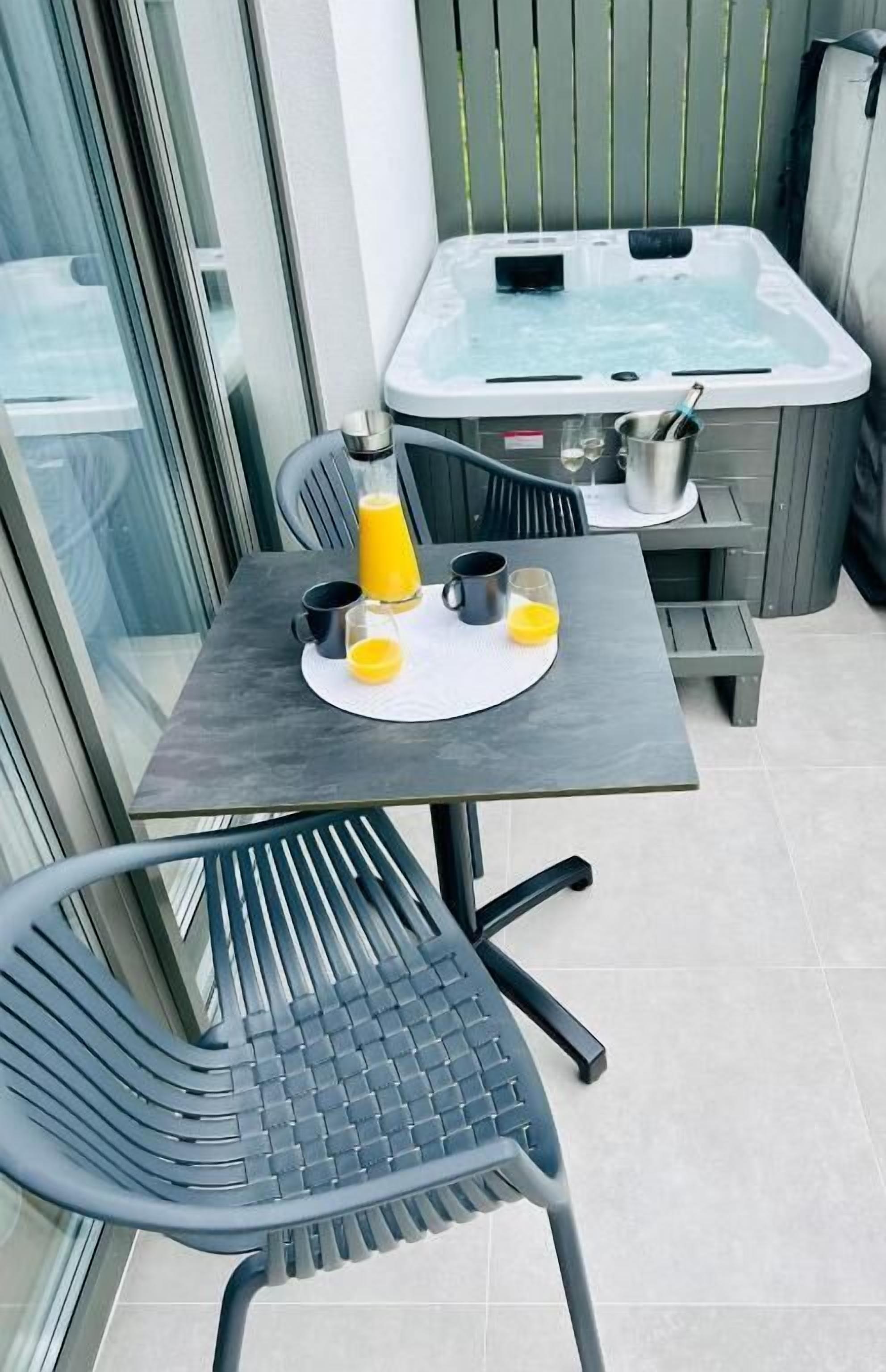 Un balcon avec une table, des chaises, un jacuzzi et une porte vitrée.