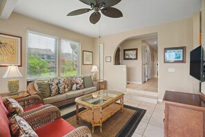 A living room with a sofa, a coffee table, wicker chairs, a ceiling fan, and a TV. - Aston Poipu Kai | Walk to Beach | Pools | Garden Views (Koloa)