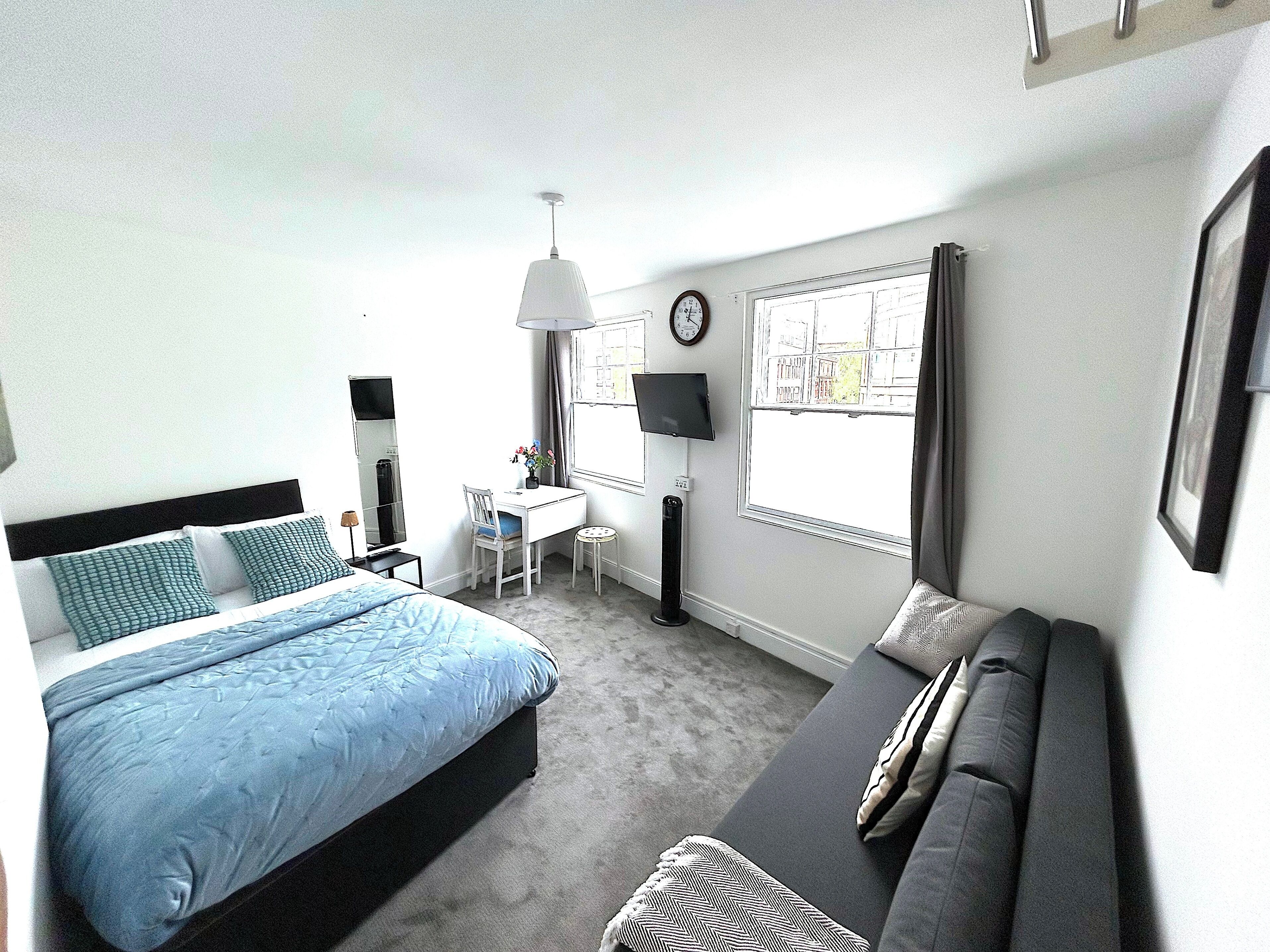 A hotel room with a bed, a desk, a chair, a TV, a window, and a sofa.