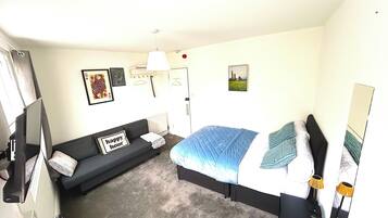 A hotel room with a bed, a sofa, a desk, and a mirror.