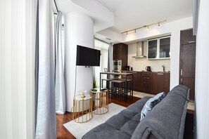 A modern living room with a grey sofa, a flat-screen TV, and a dining area with a wooden table and chairs. - Westmere Suites (Toronto)