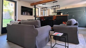Een moderne woonkamer met grijze banken, een salontafel en een keuken met donkere kasten en een balken plafond.