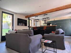 A modern living room with grey sofas, a coffee table, and a kitchen area with dark cabinets and a wooden beam ceiling. - Small townhouse in a rural seaside setting (10-minute walk to shops and the beach) (Saint-Valery-en-Caux)