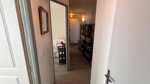 Een hal met een witte deur links, een witte wand met een lijst en een houten vloer.